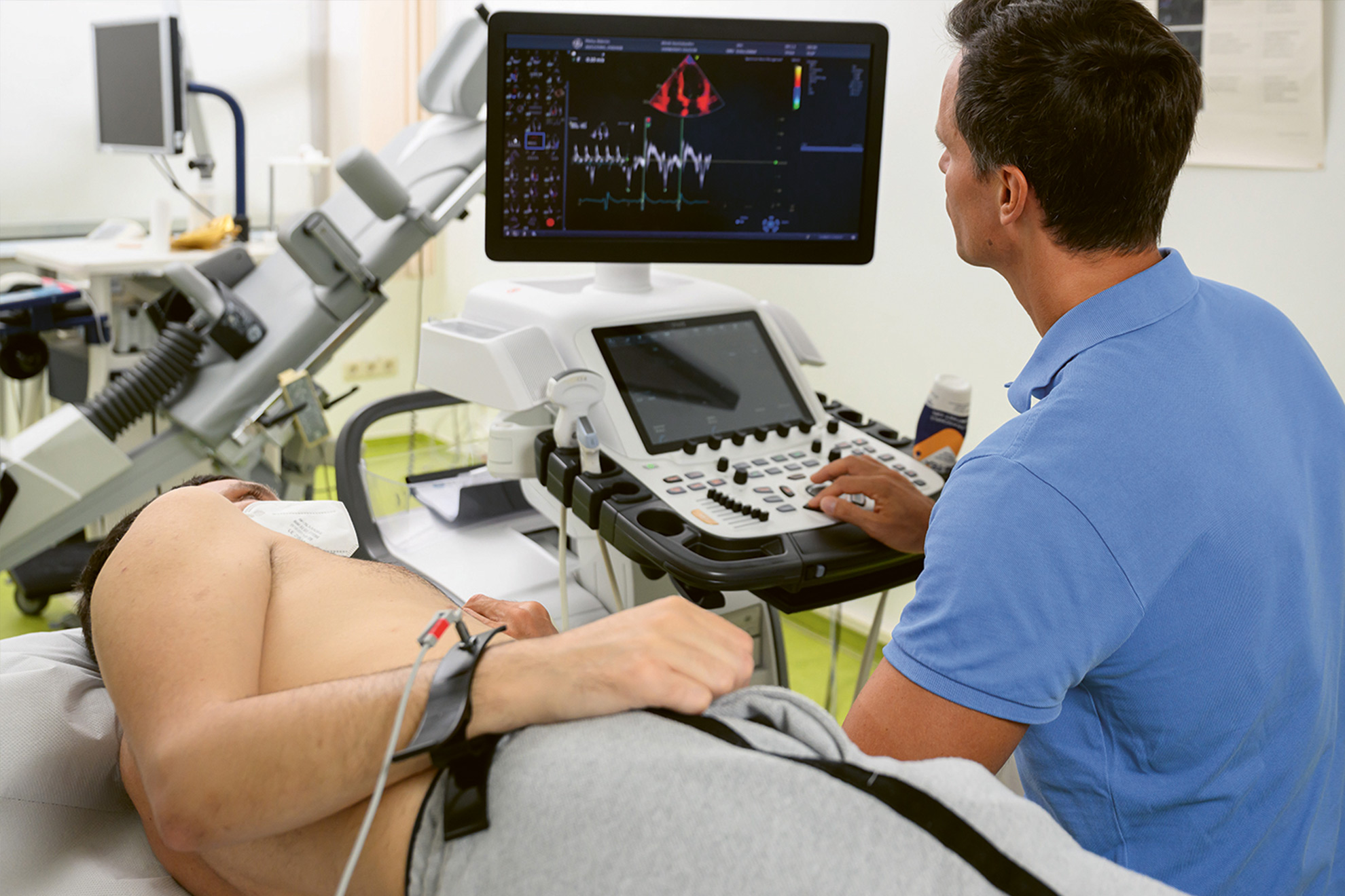 Ein Patient liegt auf einer Untersuchungsliege, während ein Arzt ein Ultraschallgerät benutzt und den Monitor betrachtet.