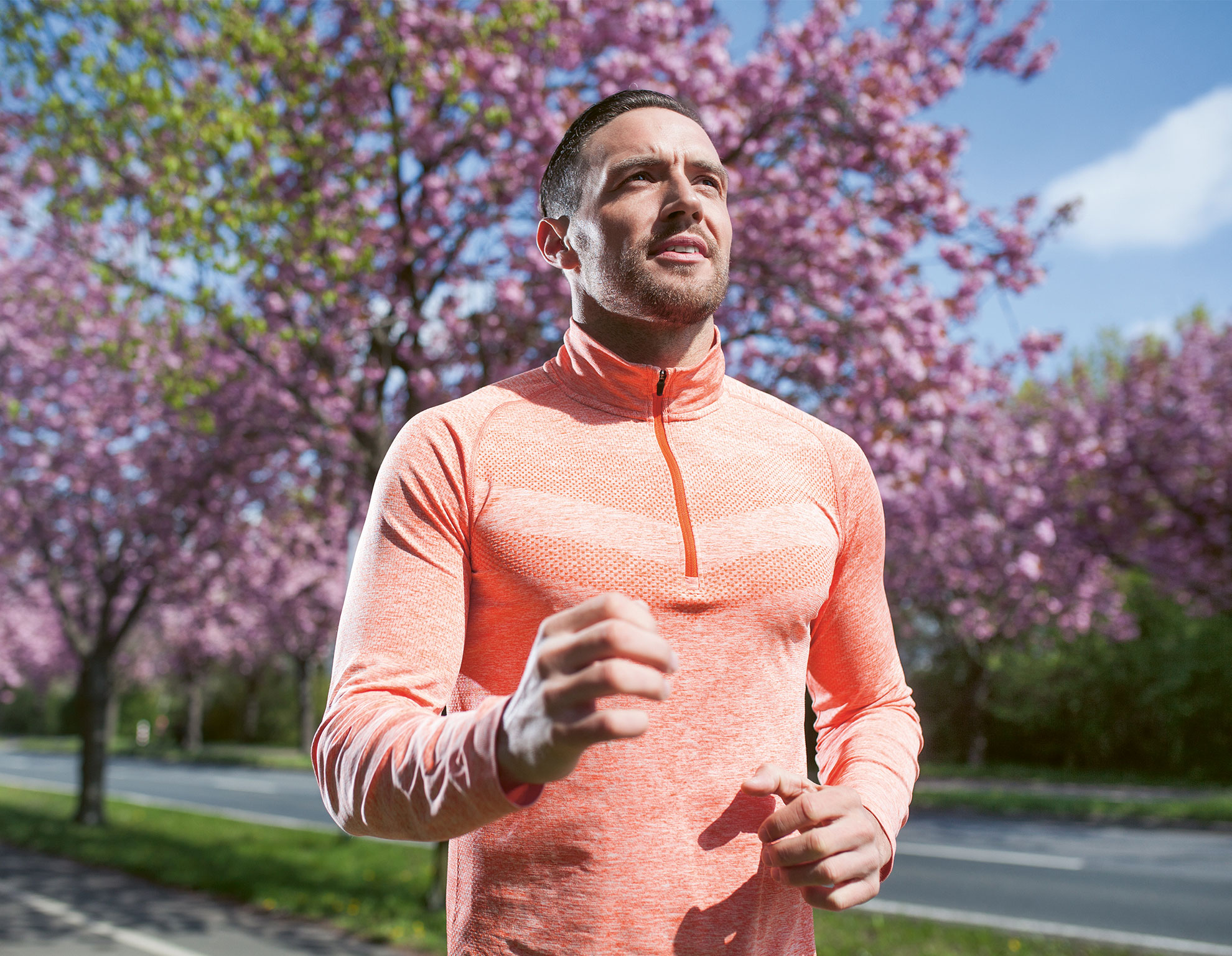 Ein sportlich gekleideter Mann joggt an einem sonnigen Tag durch einen Park, im Hintergrund blühende Bäume und ein klarer Himmel, Symbol für Bewegung und neue Lebensfreude nach einem Herzinfarkt.